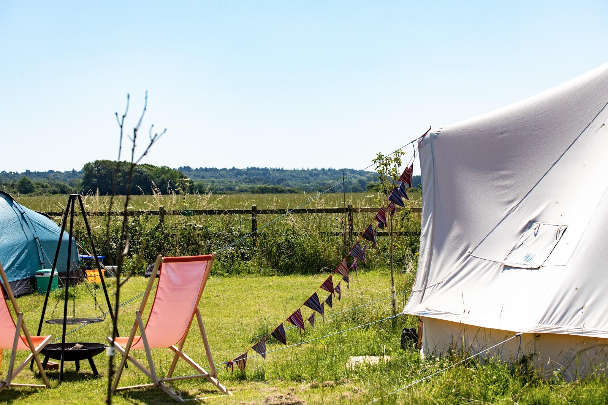 Bell tent in sunshine with a fire pit and deck chairs nearby