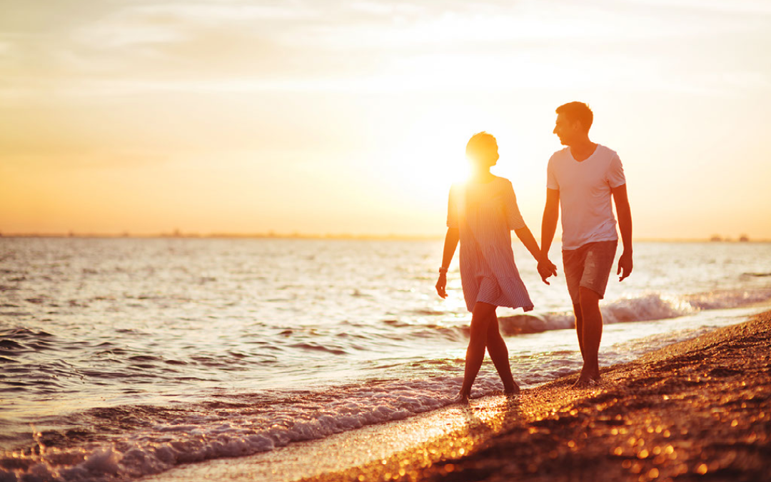 couple walking along beach at sunset