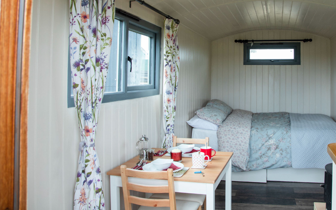 shepherds hut interior with made bed and laid out bistro dining table