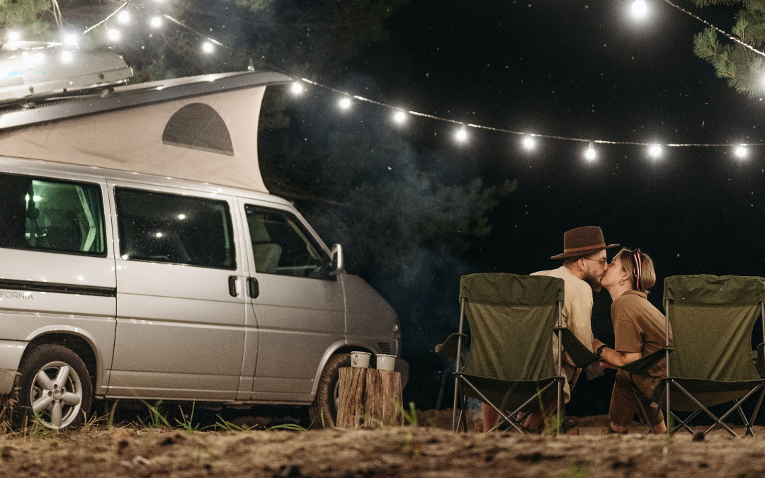 a couple kissing under fairy lights outside a campervan