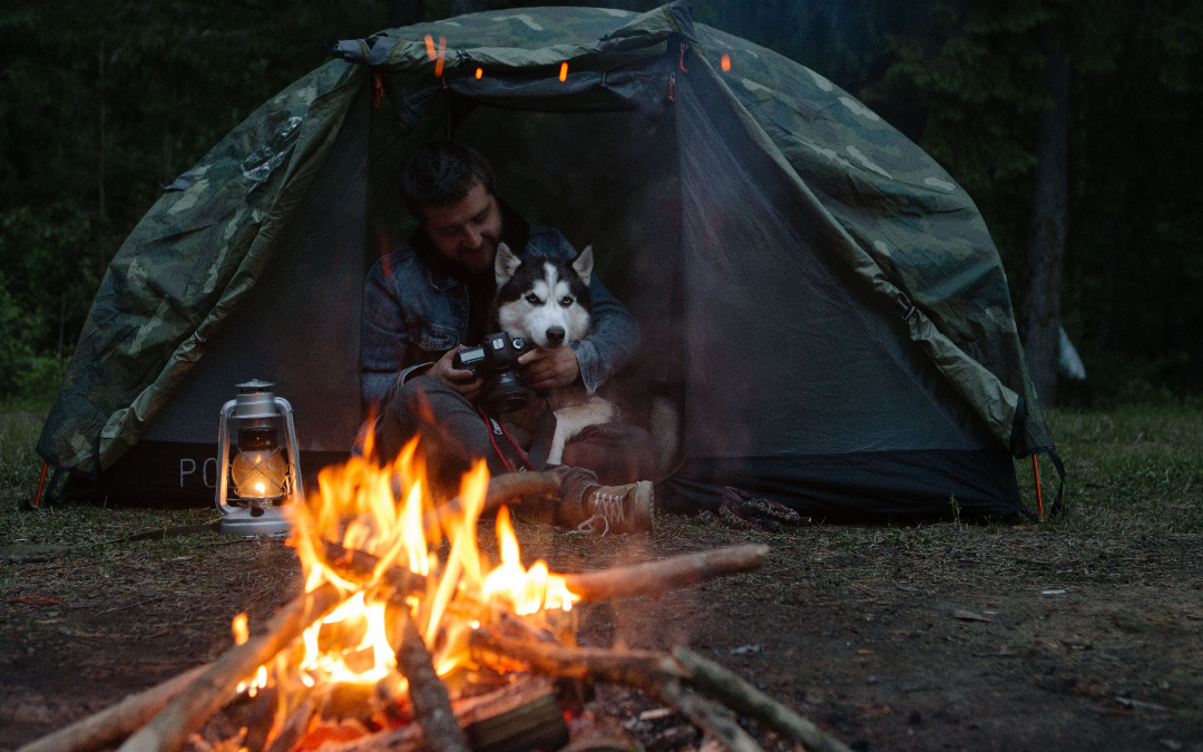 man and dog in tent with a lit campfire