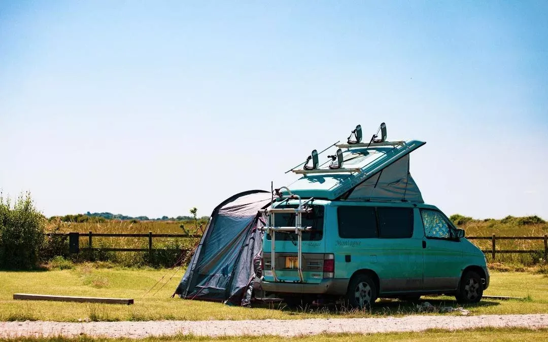a light blue campervan with awning pitched up on a campsite
