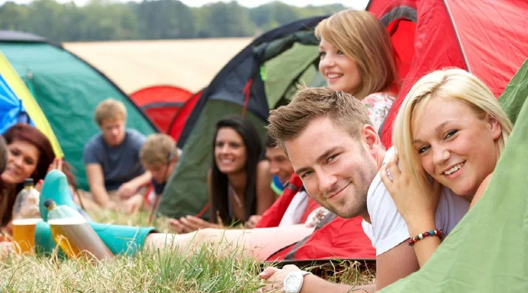 a group of young adults socialising outside their tents in a field