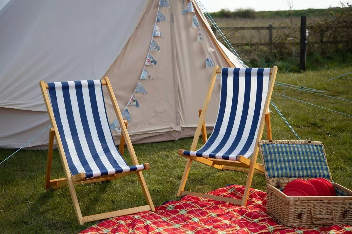 two deck chairs with a picnic setup outside of a bell tent