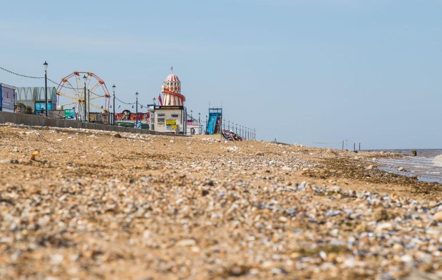 close up shot along hunstanton beach with fairground rides of rainbow park on the left