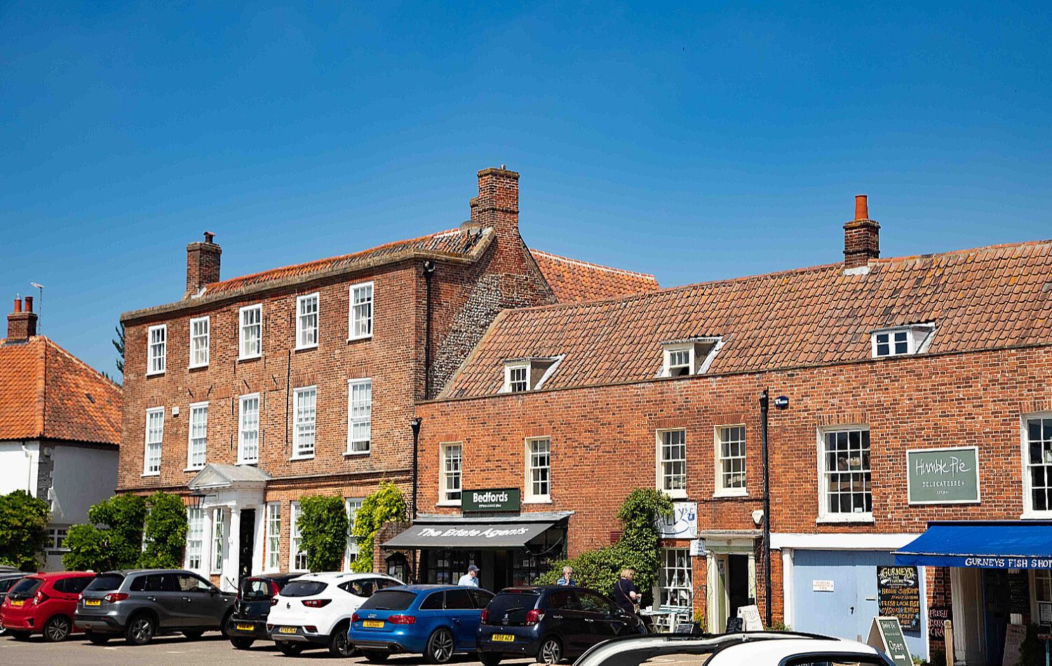 houses and shops in burnham market with cars parked out front