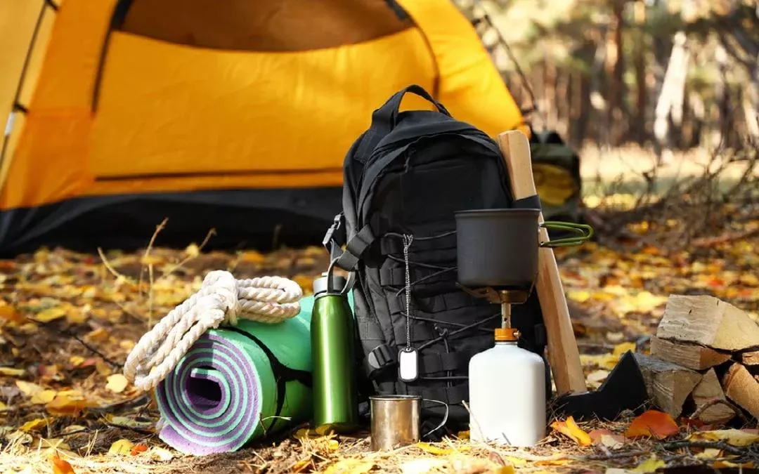 a hikers backpack with a stove and a tent in the background